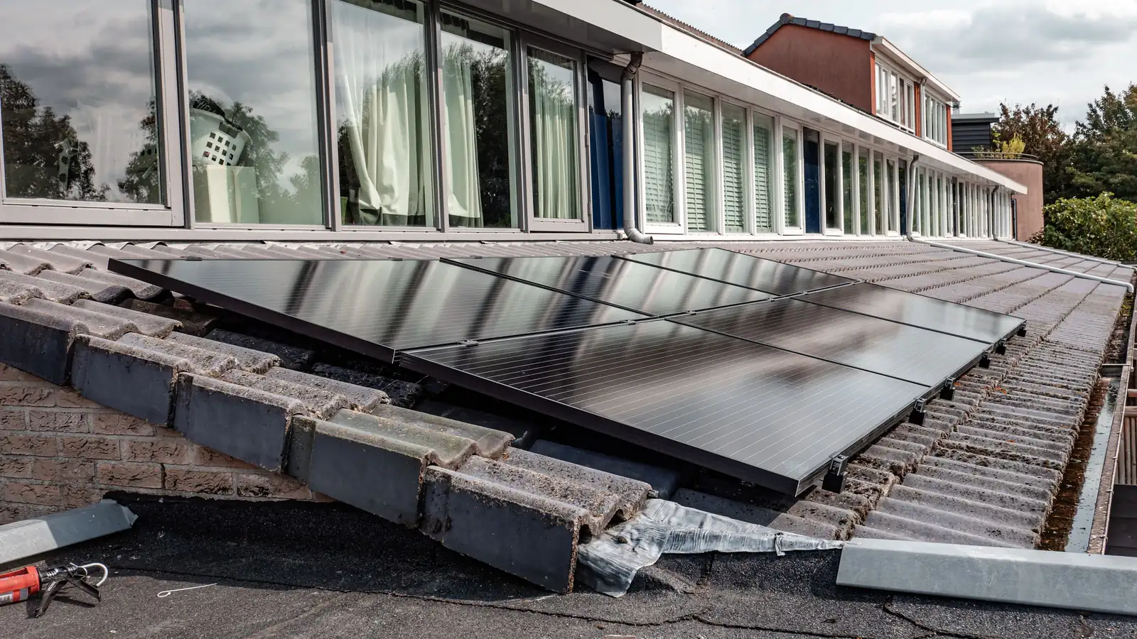 Panneaux solaires noirs posés sur le toit en tuiles d’une maison moderne aux grandes baies vitrées